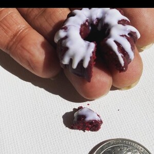 May include: A small red velvet cake doughnut with white icing. The doughnut is broken in half and a piece is missing.