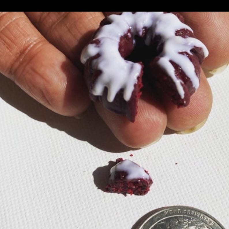 May include: A small red velvet cake doughnut with white icing. The doughnut is broken in half and a piece is missing.