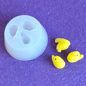 May include: A silicone mold with three cavities shaped like chicks, next to three yellow chick-shaped candies.