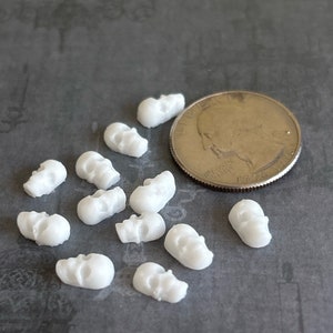 May include: A collection of 12 small white skull charms, each about the size of a US quarter.