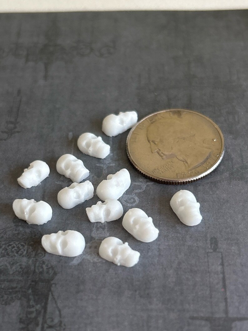 May include: A collection of 12 small white skull charms, each about the size of a US quarter.