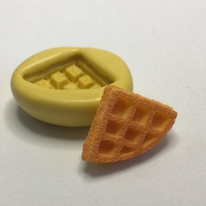 May include: A yellow silicone mold for making waffle shapes, next to a small orange waffle.