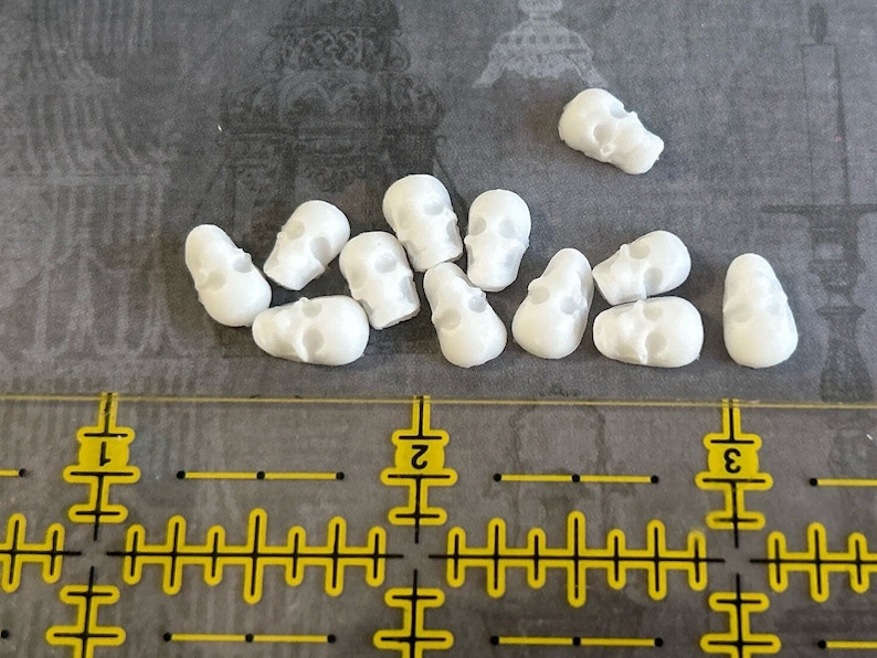 May include: A collection of 12 small white skull beads. The beads are made of a smooth, white material and have a realistic skull design.