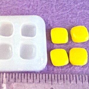 May include: A white silicone mold with four square cavities, and four yellow square resin pieces.