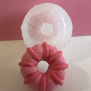 May include: A pink silicone mould for making donut-shaped pastries. The mould is shown with a pink donut-shaped pastry inside.