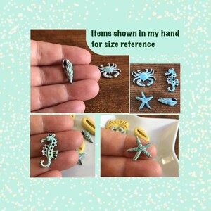 May include: A collection of small, sea-themed charms in various shapes, including a seahorse, starfish, crab, and seashells. The charms are primarily light blue and white, with a distressed finish. The text "Items shown in my hand for size reference" is visible.