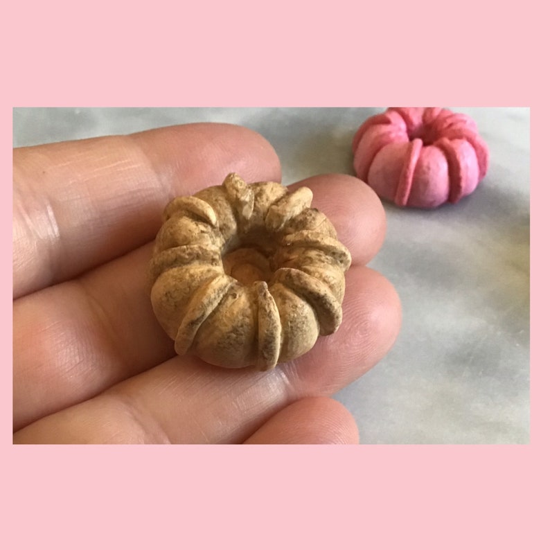 May include: A small, brown, cake-shaped doughnut with a hole in the centre. The doughnut has a textured surface and is slightly misshapen.