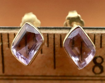 May include: A pair of gold earrings with amethyst gemstones. The gemstones are a light purple color and have a faceted cut. The earrings are shown on a ruler, with the gemstones measuring approximately 1/2 inch in length.