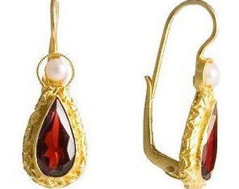 May include: Gold dangle earrings with a pear-shaped red gemstone and a small white pearl accent.