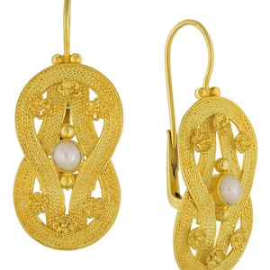 May include: Gold earrings with a pearl in the center and a delicate, intricate design. The earrings are oval shaped and have a hook closure.