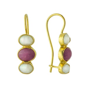 May include: A pair of gold-colored drop earrings. Each earring features three oval-shaped stones: white, magenta, and white. The earrings have a hook closure. The earrings are displayed against a white background.