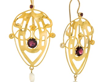May include: A pair of gold earrings with a delicate, intricate design. Each earring features a red gemstone surrounded by a gold frame and a dangling pearl.