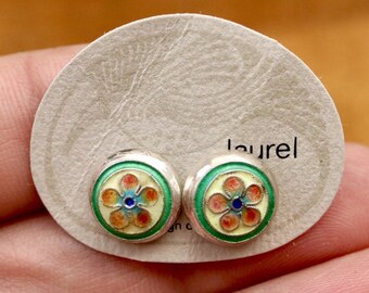 Könnte beinhalten: Ein Paar silberne Ohrstecker mit einem Blumenmuster aus grünem, gelbem, orangefarbenem und blauem Emaille. Die Ohrringe befinden sich auf einer weißen Karte mit dem aufgedruckten Wort "laurel".