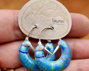 Può includere: Un paio di orecchini a cerchio in argento con smalto blu, verde e arancio. Gli orecchini hanno la forma di uccelli con un design ad occhio stilizzato. Gli orecchini sono su una carta che dice "laurel san francisco".