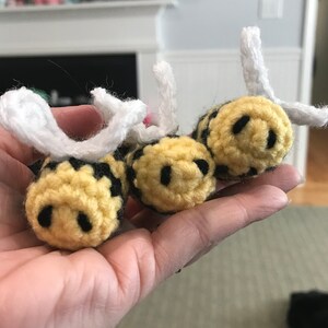 Pode incluir: Três brinquedos de abelha de crochê com listras amarelas e pretas e asas brancas. As abelhas têm rostos sorridentes pretos.