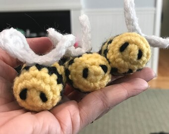 May include: Three crocheted bee toys with yellow and black stripes and white wings. The bees have black smiling faces.