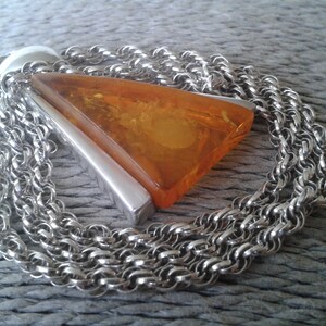 May include: A silver chain necklace featuring a triangular amber pendant. The pendant is accented with a silver bar. The chain is composed of multiple strands of small, interlocking links.