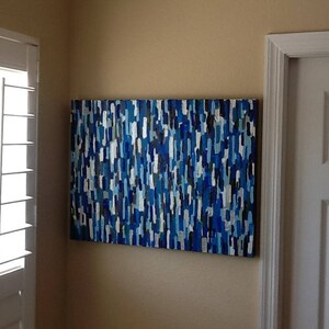 May include: Abstract painting with blue, white and black vertical stripes. The painting is hanging on a wall in a room with white trim.