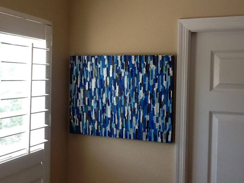 May include: Abstract painting with blue, white and black vertical stripes. The painting is hanging on a wall in a room with white trim.