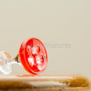 May include: A miniature red glass martini glass with a clear stem, lying on its side on a wooden surface.