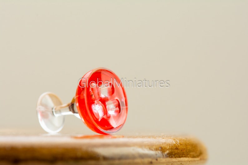 May include: A miniature red glass martini glass with a clear stem, lying on its side on a wooden surface.