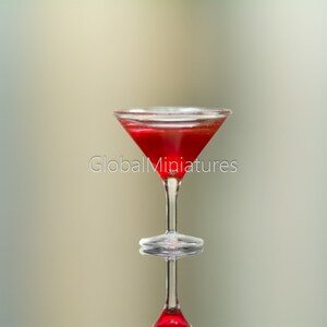 May include: A clear glass martini glass filled with a red liquid. The glass is sitting on a reflective surface.