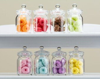 May include: Ten clear glass jars with lids filled with colorful pastel-colored candy. The jars are arranged in two rows of five on a white shelf.