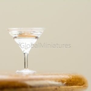 May include: A clear glass martini glass filled with liquid sits on a wooden surface.