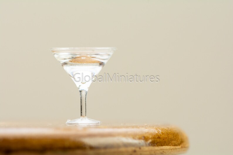 May include: A clear glass martini glass filled with liquid sits on a wooden surface.