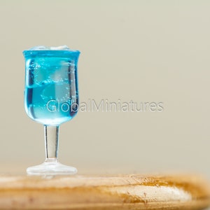 May include: A miniature glass filled with blue liquid and ice cubes, sitting on a wooden surface.