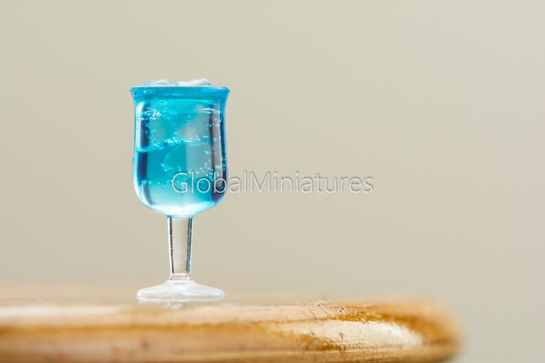 May include: A miniature glass filled with blue liquid and ice cubes, sitting on a wooden surface.