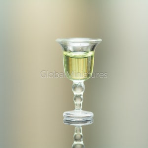 May include: A clear glass goblet with a round base and a stem with a series of small spheres. The goblet is filled with a light yellow liquid.