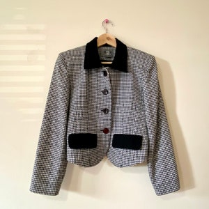 Peut inclure: Un blazer en tissu à motif pied-de-poule noir et blanc avec un col et des poches en velours noir. Le blazer a une fermeture à boutons et est sur un cintre.