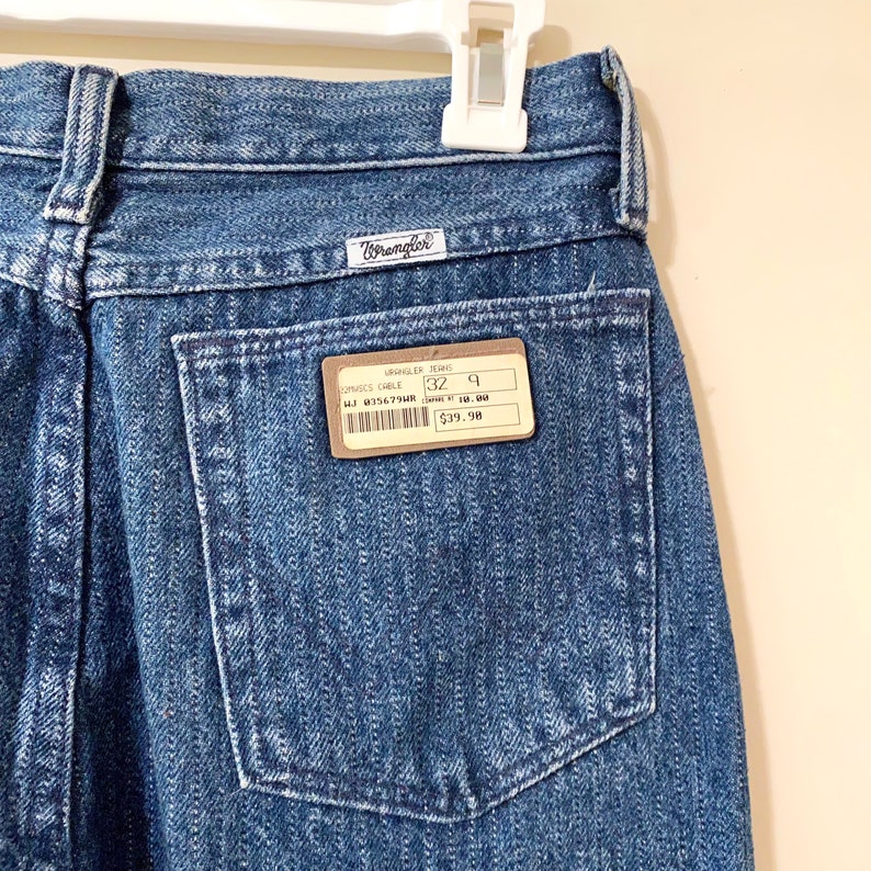 May include: A pair of blue denim Wrangler jeans with a brown price tag that reads "Wrangler Jeans, Original Chele, 32, 9, 41J 8356794R, $39.98".