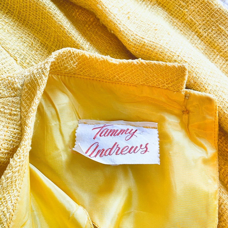 K&ouml;nnte beinhalten: Nahaufnahme eines gelben Stofflabels mit dem Text "Tammy Andrews" in roter Kursivschrift.