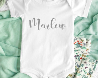May include: White baby onesie with the name "Marlow" written in gray cursive lettering.