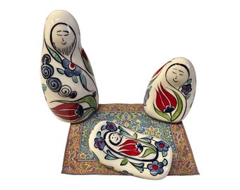 May include: Ceramic nativity scene with three figures and a rug. The figures are painted in a white, blue, red, and green floral pattern. The rug is a colorful patterned rug.