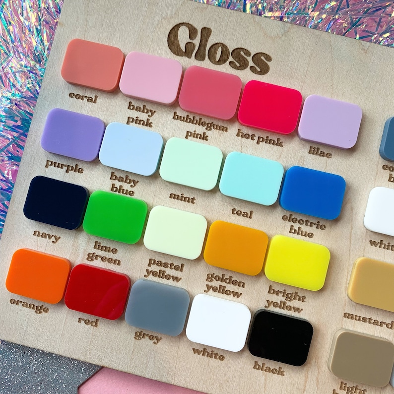 May include: A wooden color chart labeled "Gloss" displays an array of colorful, rectangular acrylic samples. Colors include coral, baby pink, bubblegum pink, hot pink, purple, baby blue, mint, teal, electric blue, orange, red, grey, white, and black.