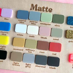 May include: A wooden display board with the word "Matte" engraved at the top. It features an array of small, rectangular color swatches in various shades, including blue, green, pink, and brown, with color names below each swatch.