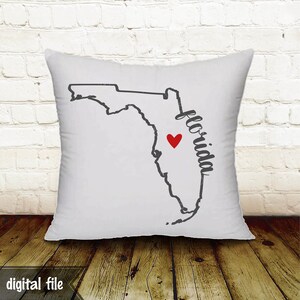 May include: White square pillow featuring a black outline of the state of Florida with a red heart marking a location. The word "Florida" is written in a script font. The words "digital file" are at the bottom.