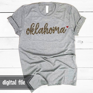 May include: Gray t-shirt with the word "oklahoma" in a leopard print font with a small red heart next to it.