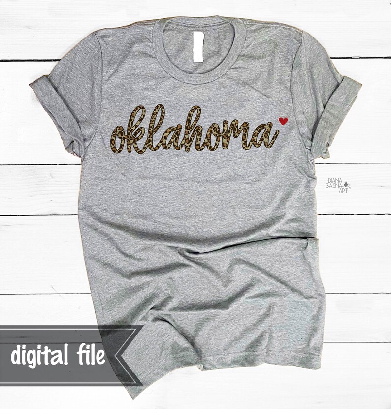 May include: Gray t-shirt with the word "oklahoma" in a leopard print font with a small red heart next to it.