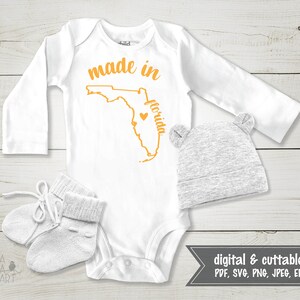 May include: White baby bodysuit with long sleeves, featuring the text "made in florida" in orange, along with a Florida outline and heart. Includes a gray beanie with bear ears and white baby booties. Digital and cuttable files.