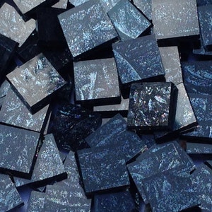 May include: A pile of small, square, iridescent blue glass tiles. The tiles have a dark blue base with a light blue iridescent sheen.