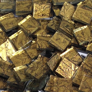 May include: A pile of small, square, gold-colored glass tiles with a metallic finish. The tiles have a textured surface and are perfect for crafting projects.