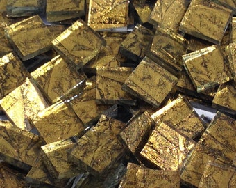 May include: A pile of small, square, gold-colored glass tiles with a metallic finish. The tiles have a textured surface and are perfect for crafting projects.