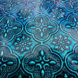 May include: A close-up of a teal blue and black patterned fabric with a repeating geometric design. The fabric has a textured, embossed look.