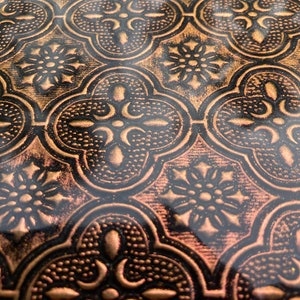 May include: Close-up of a textured, embossed surface with a repeating pattern of gold and black quatrefoils. The surface has a glossy finish.
