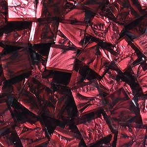 May include: A pile of small, square, red glass tiles with a metallic finish. The tiles have a swirling, textured pattern.