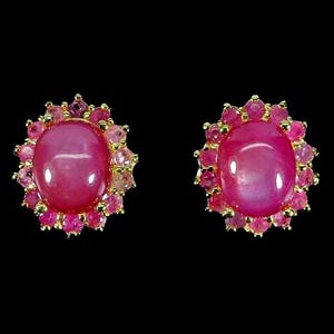 Pode incluir: Um par de brincos com uma grande pedra preciosa rosa de corte cabochão oval no centro, rodeada por um halo de pedras cor-de-rosa mais pequenas de corte redondo cravadas numa armação de metal dourado sobre um fundo preto sólido.